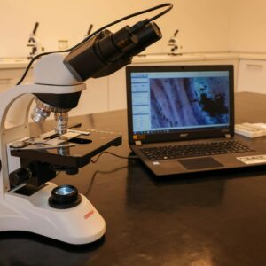 Close-up of a microscope connected to a laptop in a laboratory environment.